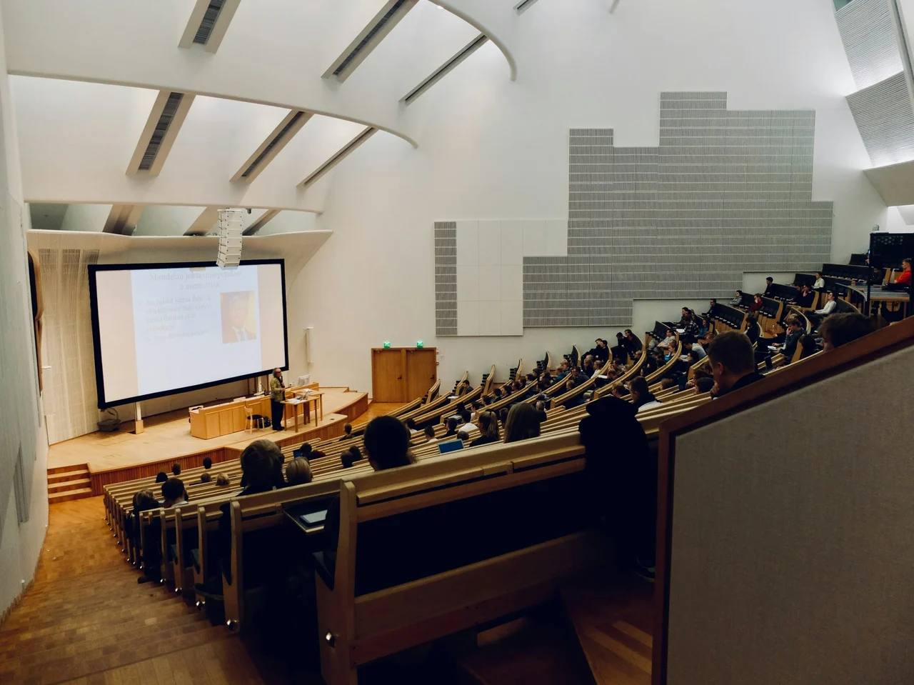 Large university lecture hall with students seated and watching a professor