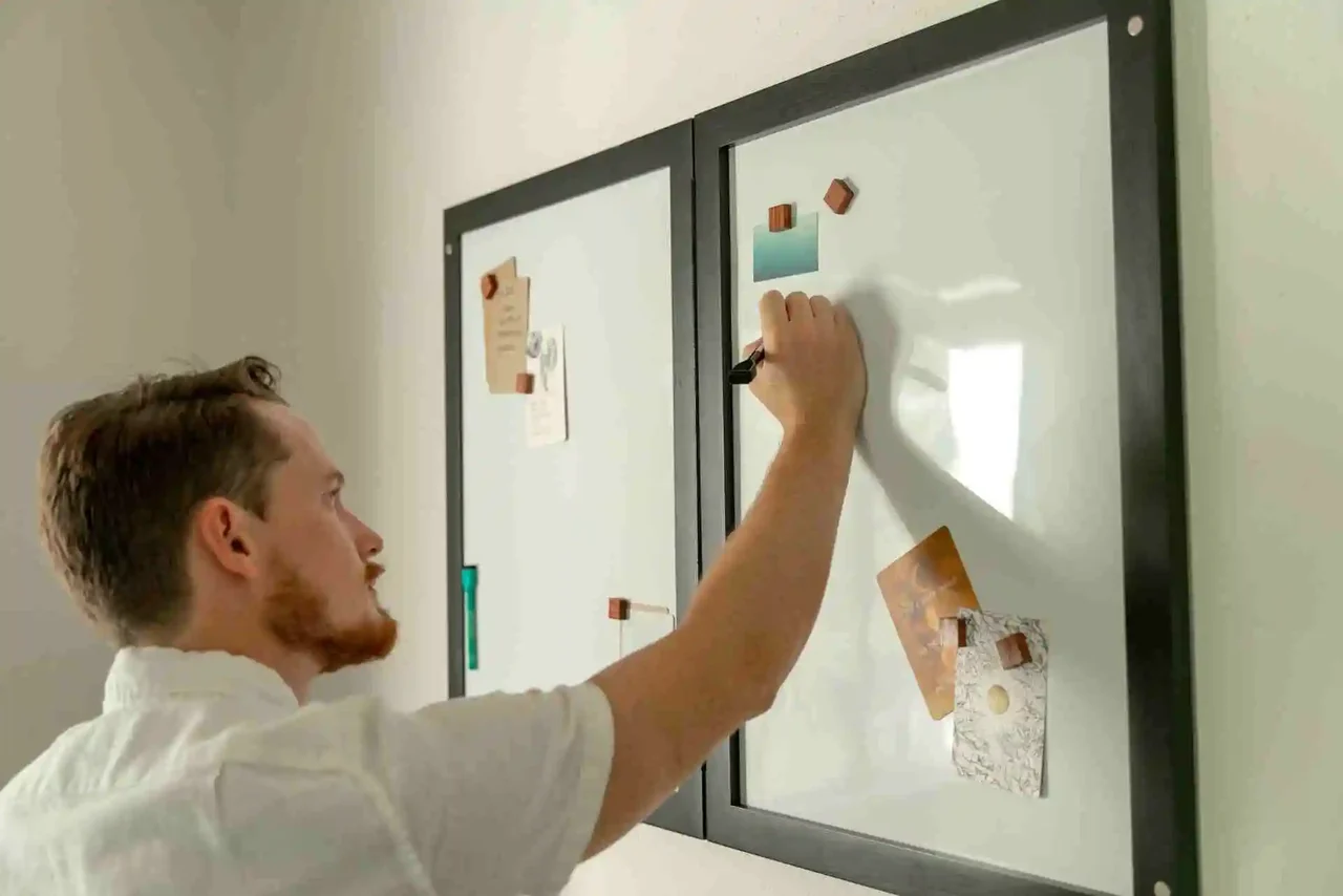 Man sketching or writing notes on a whiteboard with magnets and paper. 