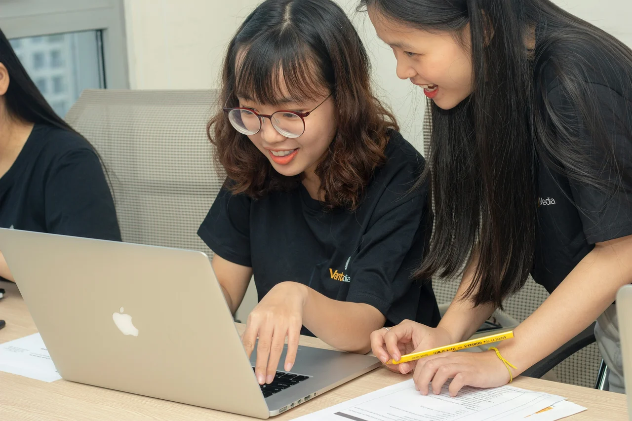 Two smiling students working together on a laptop at a desk.